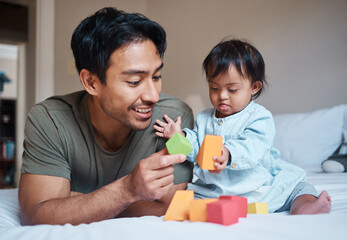 Baby, down syndrome and learning on a bed with child and father playing with educational blocks in...