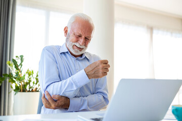 Shot of a businessman holding his elbow in pain while seated at his desk, hand pain