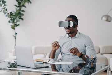 African american businessman uses virtual reality glasses working in cyberspace at laptop in office