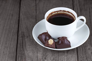Fototapeta premium White cup of coffee with chocolates on a saucer on a wooden background