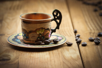 Old vintage copper cup with roasted coffee beans on wooden background
