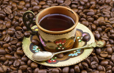 Traditional painted copper cup of coffee with heap of roasted coffee beans