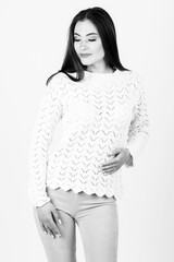 Beautiful long hair woman studio portrait with white sweater and tight trousers. Model looking aside the camera with smile. Image contains motion blur and noise. Black and white image
