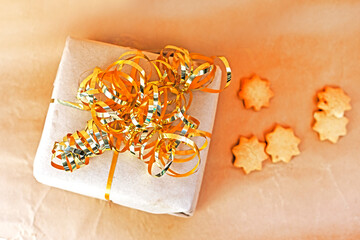 New Year's gift wrapped in craft paper with a gold ribbon and Christmas cookies, congratulations.
