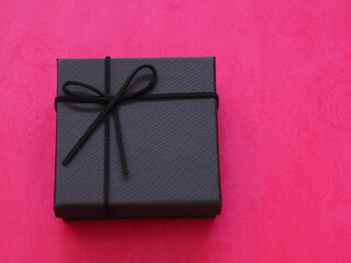 Black gift box with black bow on red paper background. Holiday season concept. Top view, flat lay with copy space..