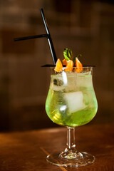 Green Alcoholic cocktail decorated with mandarin slices on the bar counter of a cafe