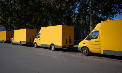 A fleet of yellow electric delivery vans parking in front of green trees.