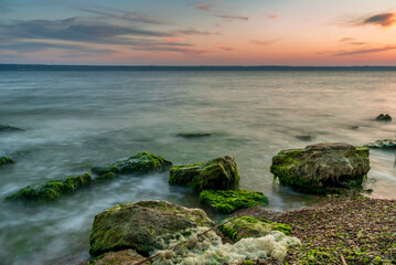 Green mossy stones lay on the shoreline while the sun is setting down