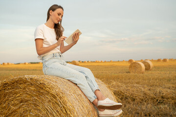 Woman sitting on a haystack and using a tablet. 