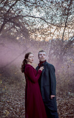 Vampire man wearing victorian suit with vampire woman in the autumn forest in the fog. Vintage...