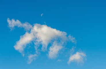 There is a moon and white clouds in the blue sky