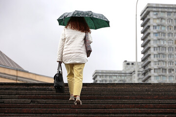 Woman with umbrella walking up the steps on city buildings background. Rain in autumn city