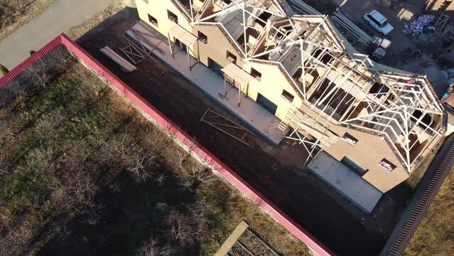 Aerial view of unfinished brick house with wooden roof frame structure under construction.