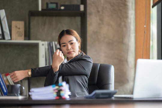 Asian businesswoman, attractive and young, stretching her shoulder and arm muscles. due to sitting and working for a long time, to business people and office syndrome concept.