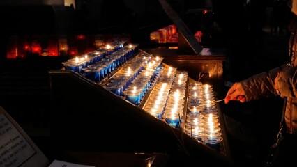 Person's hand lightning candles from a stand in the church