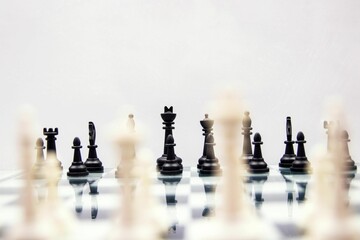 Selective focus of chess pieces on a glossy chessboard on white background