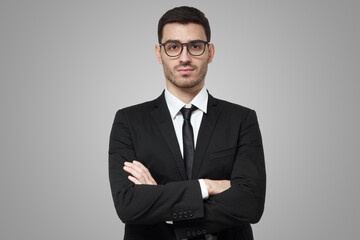 Serious young business man in suit standing against grey background with crossed arms