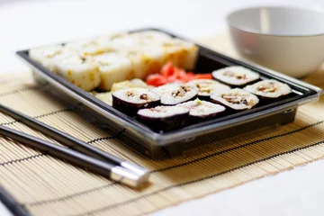 Foto op Plexiglas Set of red ginger rolls with a soy sauce bowl and black chopsticks on a bamboo mat © Ruslan Kolodenskiy/Wirestock Creators