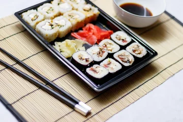 Fotobehang Set of red ginger rolls with a soy sauce bowl and black chopsticks on a bamboo mat © Ruslan Kolodenskiy/Wirestock Creators