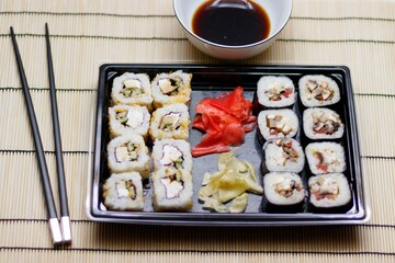 Set of red ginger rolls with a soy sauce bowl and black chopsticks on a bamboo mat