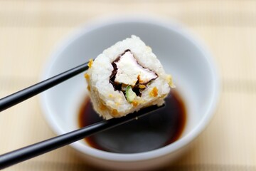 Japanese food roll picked up with black chopsticks with a soy sauce bowl in the background