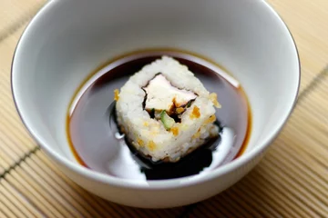 Foto op Plexiglas Japanese food roll in a soy sauce bowl on a bamboo mat © Ruslan Kolodenskiy/Wirestock Creators