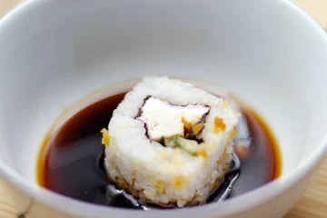 Foto op Plexiglas Japanese food roll in a soy sauce bowl on a bamboo mat © Ruslan Kolodenskiy/Wirestock Creators