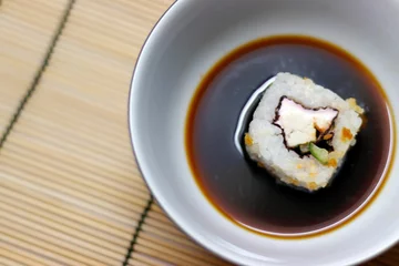Fotobehang Japanese food roll in soy sauce bowl on a bamboo mat © Ruslan Kolodenskiy/Wirestock Creators