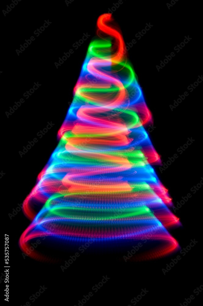 Wall mural glowing colorful design of wavy lines in the shape of a christmas tree on black background