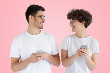 Excited couple, man and woman smiling, looking at each other while both using mobile phones