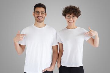 Daylight shot of smiling couple pointing at blank white t-shirts with finger, copy space for ads