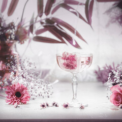 Fancy drink in wide glass of champagne with pink ice cubes and and purple flowers and leaves.