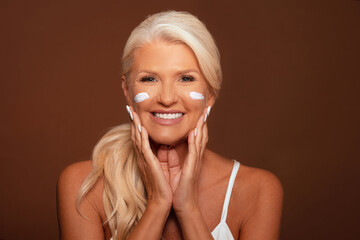 Portrait of a beautiful mature woman with beautiful skin, standing over a brown background 