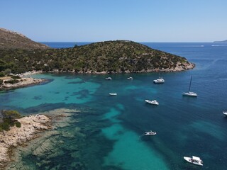 Aerial view of Cala Moresca and Figarolo Island in Golfo Aranci, north Sardinia. Birds eye from above of yacht, boats, crystalline and turquoise water. Tavolara Island in the background, Sardegna.