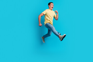 Fototapeta na wymiar Full length photo of excited young man in t-shirt jumping running hurry discounts isolated over blue background