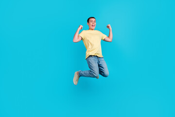 Fototapeta na wymiar Full length photo of excited young man in t-shirt jumping while celebrating success isolated over blue color background