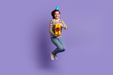 Full length body photo of cheerful positive girl holding wrapped box jumping up isolated vivid purple color background