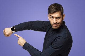 Man pointing at watch with impatience as if asking to hurry up, isolated on purple background