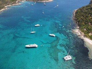 Aerial view of Cala Moresca and Figarolo Island in Golfo Aranci, north Sardinia. Birds eye from above of yacht, boats, crystalline and turquoise water. Tavolara Island in the background, Sardegna.