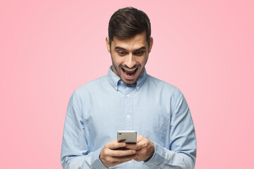 Young businessman looking at phone with surprise expression, isolated on pink background