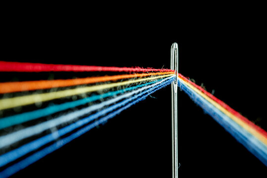 multi-colored threads for sewing in the form of a rainbow pass through an antique needle on a black background