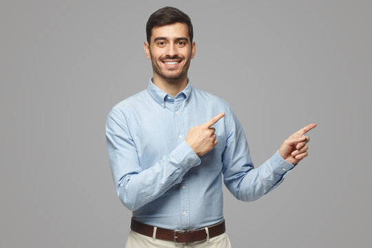 Smiling Businessman Pointing Right With Two Hands Looking At Camera, Isolated On Gray