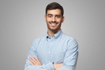 Modern businessman in blue shirt standing with crossed arms, isolated on gray