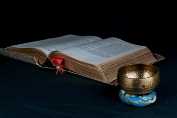 Closeup of Tibetan bell and an old spiritual book isolated on black background