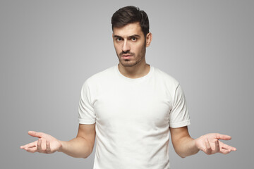 Young man spreading hands not knowing what to do, isolated on gray