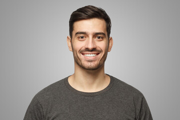 Portrait of smiling handsome young man in casual t-shirt, isolated on gray