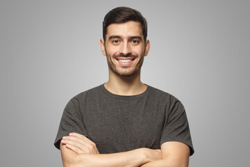 Portrait of smiling handsome man in grey t-shirt standing with crossed arms on gray background