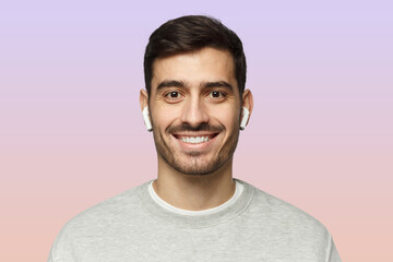 Close-up portrait of young smiling handsome man with earphones isolated on pink