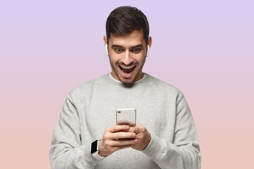 Young excited man looking at phone with surprise, isolated on pink background