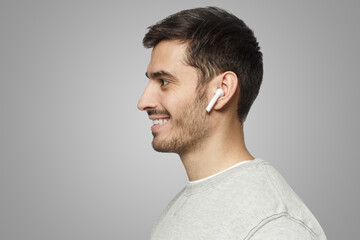 Obraz premium Sideways portrait of smiling man listening to music or radio in modern wireless earphones